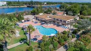 An aerial view of a resort with a swimming pool, lounge chairs, and a tennis court.