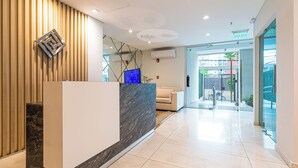 A modern reception area with a marble reception desk, a wooden slat wall, and a glass door leading outside. - Sky Stays at Agora Villamorra (Asunción)