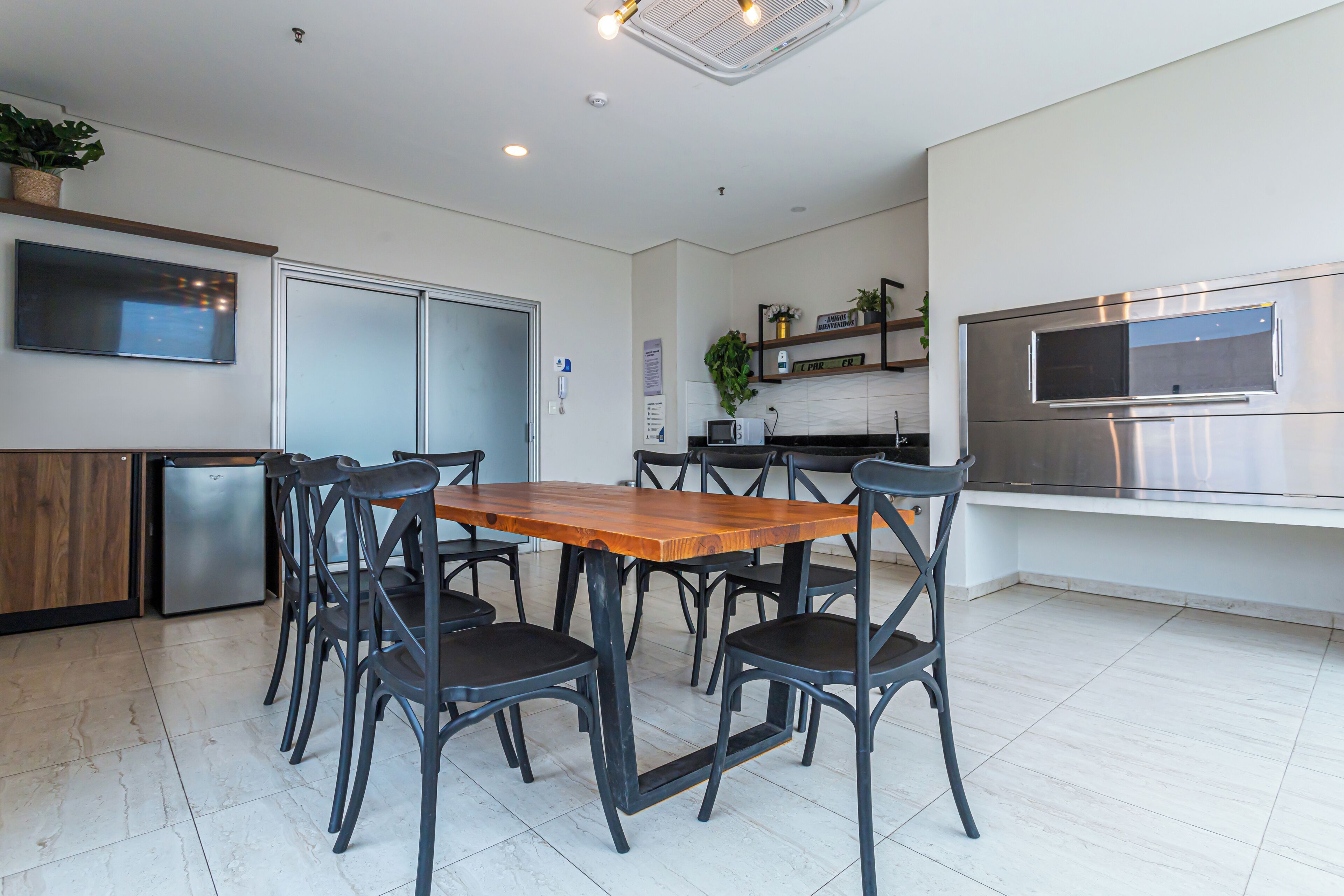 A modern kitchen with a wooden dining table, black chairs, a built-in microwave, and a stainless steel oven.