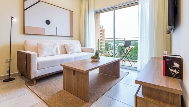 A modern living room with a sofa, coffee table, and a flat-screen TV mounted on the wall. - Sky Stays at Agora Villamorra (Asunción)