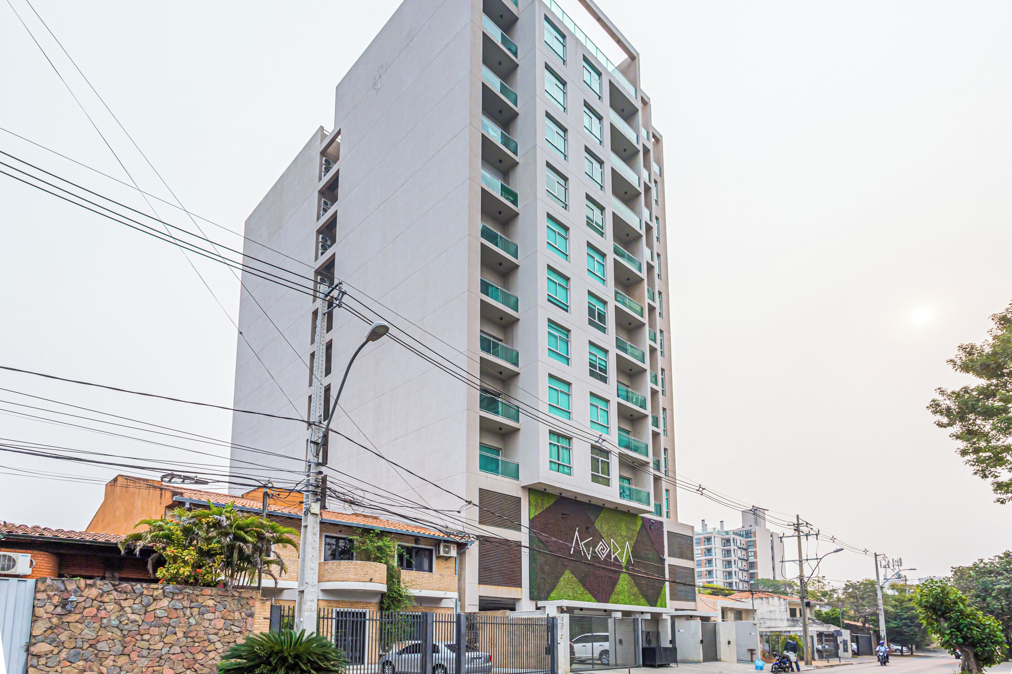 Un edificio residencial alto con múltiples balcones, una pared de piedra con vegetación y una entrada visible.