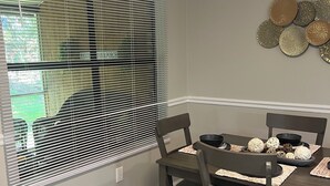 A dining area with a table set for four, a window with blinds, and decorative wall art. - NEW! Charming 2-bedroom townhome in convenient location (North Charleston)