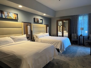 A hotel room with two beds, a sitting area with a chair, a small table, and artwork on the walls.