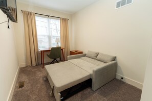 Una habitación pequeña con una cama individual, un escritorio, una silla y una ventana con cortinas.