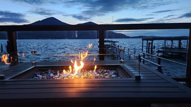 Eine Terrasse mit Feuerstelle mit Blick auf ein Gewässer und entfernte Berge.