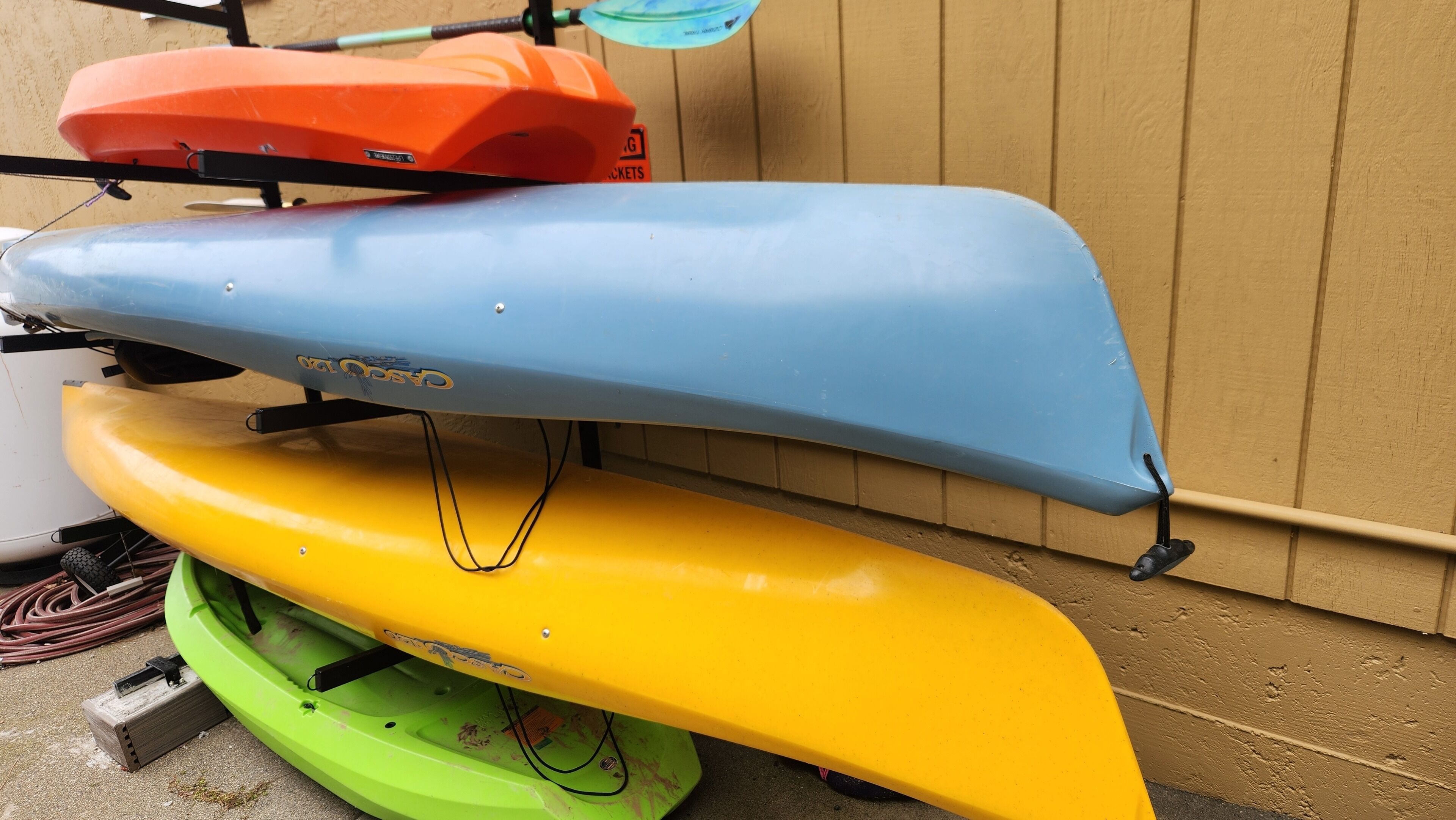 Three kayaks of different colors stacked on a stand.