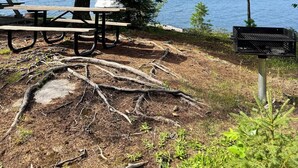 A lakeside campsite with a picnic table, a grill, and a bench. - Couples Wilderness Suite (Cook)