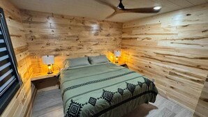 A wooden-paneled room with a bed, two bedside lamps, and a ceiling fan. - Couples Wilderness Suite (Cook)
