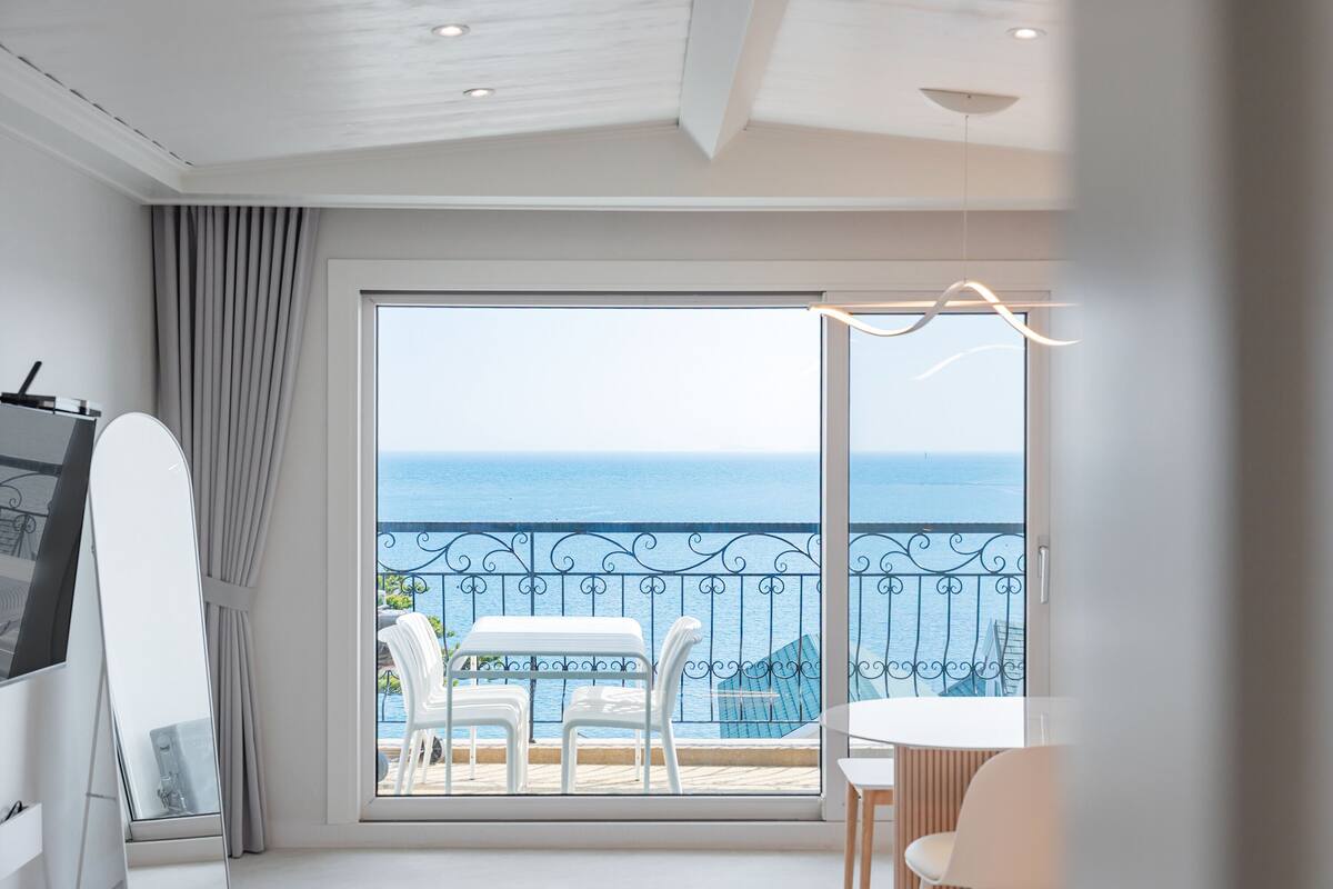 A modern room with a large sliding glass door leading to a balcony with a view of the sea.