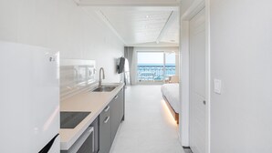 A modern kitchen with a large island, a built-in oven, and a view to a balcony with a railing. - Ocean The Hill (Taean)