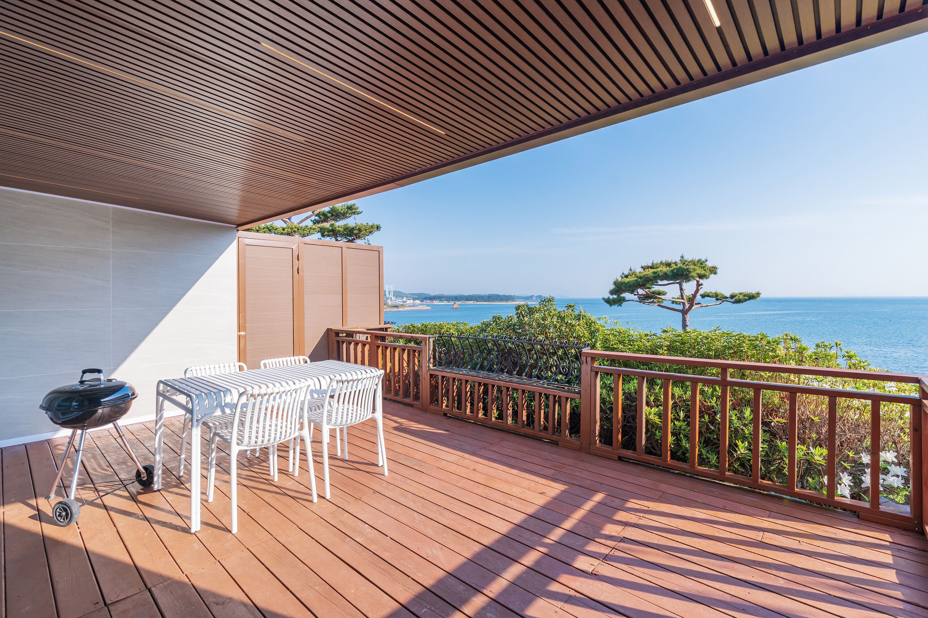 Um deck de madeira com mesa, cadeiras, churrasqueira e vista para o mar.