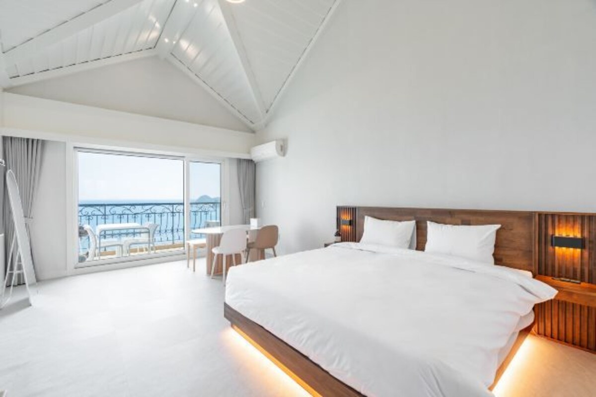 A hotel room with a large bed, a desk, and a balcony with a view.
