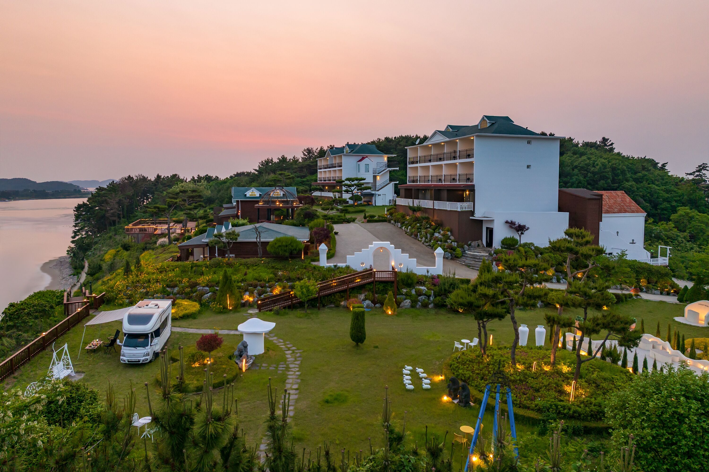 A resort with multiple buildings, a grassy area with a parked RV, and a view of the water.