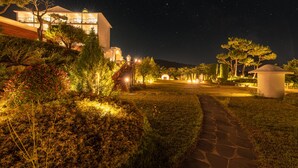 A nighttime view of a well-lit hotel with a pathway leading to a building, surrounded by landscaped gardens and trees. - Ocean The Hill (Taean)