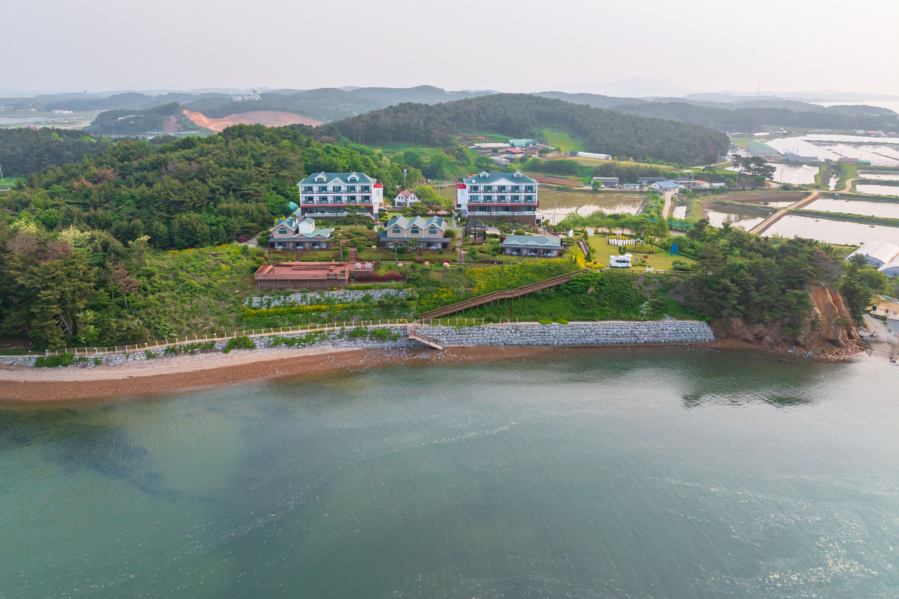A coastal hotel with multiple buildings, a bridge, and a body of water.