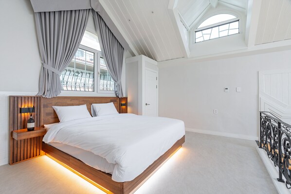 A modern bedroom with a large bed, wooden headboard, and a skylight. - Ocean The Hill (Taean)