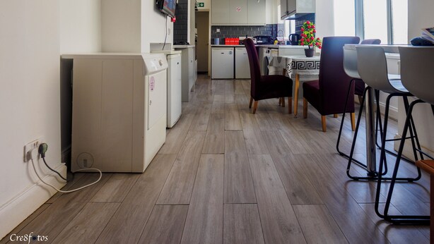 A modern kitchen with a dining area, wooden flooring, and a TV mounted on the wall. - WoodHus Lodge  Large Double Room 3 (Stoke-on-Trent)
