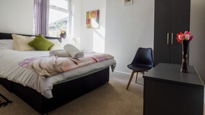 A neatly made bed with pillows, a bedside table with a vase of flowers, and a wardrobe. - WoodHus Lodge  Large Double Room 3 (Stoke-on-Trent)