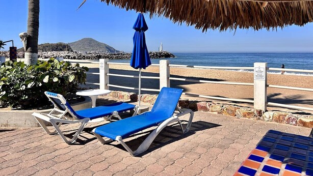 Un espace de détente aménagé sur la plage, avec deux chaises longues bleues et un parasol en chaume.