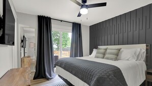 A modern bedroom with a bed, a wooden nightstand, a ceiling fan, and a view of the outdoors through large windows. - Zest of Zionsville with WiFi, AC (Zionsville)