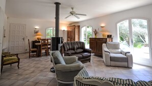 Een ruime woonkamer met een open haard, leren banken en een groot raam met uitzicht op groen.