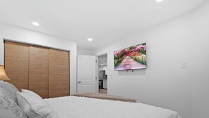 Une chambre à coucher comprenant un lit, une armoire, un tableau et une porte donnant sur la cuisine.