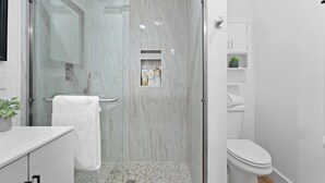 Une salle de bain moderne avec une douche à parois de verre, des toilettes blanches et une petite étagère contenant des articles de toilette.
