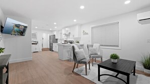 Une cuisine moderne avec des meubles blancs, un îlot central et un coin repas comprenant une table et des chaises.