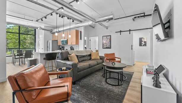 Un salon moderne avec un canapé, des fauteuils, une table à manger et un coin cuisine à l’arrière-plan.
