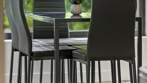 Un coin repas avec une table et des chaises, une plante en pot et une vue sur la verdure grâce à de grandes fenêtres.