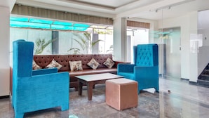 Een moderne lobby met een bruine leren bank, twee blauwe fauteuils, een houten salontafel en een gestreept voetenbankje.