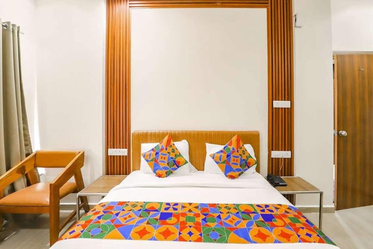 Una habitación de hotel con una cama, dos almohadas, una mesita de noche, una silla y un armario.