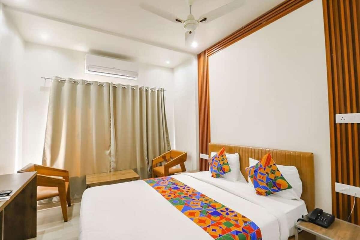 Habitación de hotel con cama, escritorio, silla, ventilador de techo y ventana con cortinas.