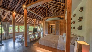 Un'ampia stanza con un letto grande, travi in legno al soffitto, una scrivania con una sedia e un muro decorato con maschere.