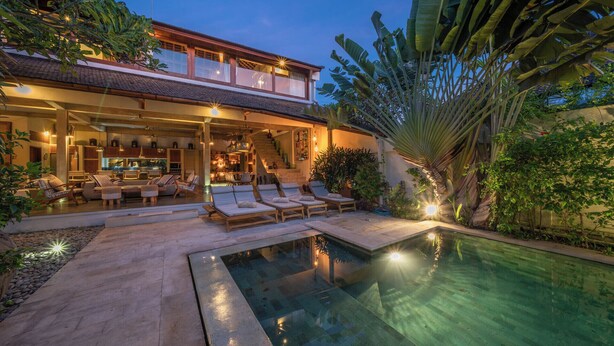 Una casa a due piani con piscina, area relax esterna e rigogliosa vegetazione tropicale.