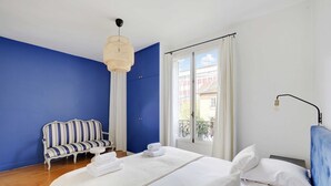 Un dormitorio con una cama, una pared azul, un sofá a rayas y una ventana con cortinas.