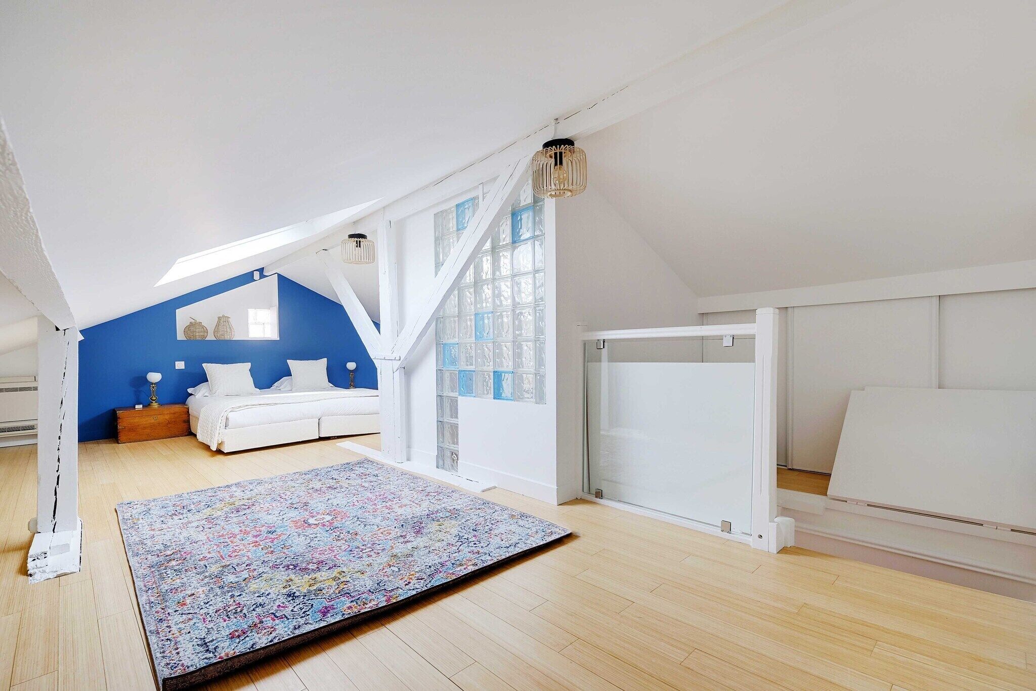 A bedroom with a sloped ceiling, a large window, a bed, a nightstand, and a colorful rug.
