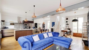 Una sala moderna con un sofá seccional azul, una mesa de centro y lámparas colgantes.