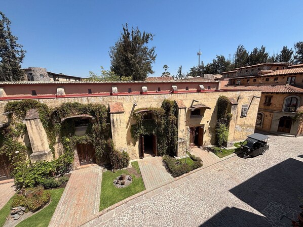 A courtyard with stone buildings, arched doorways, and a paved area with a vehicle.