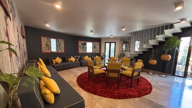 Un salon moderne avec un canapé, des fauteuils jaunes, un tapis rouge et des œuvres d’art accrochées aux murs.