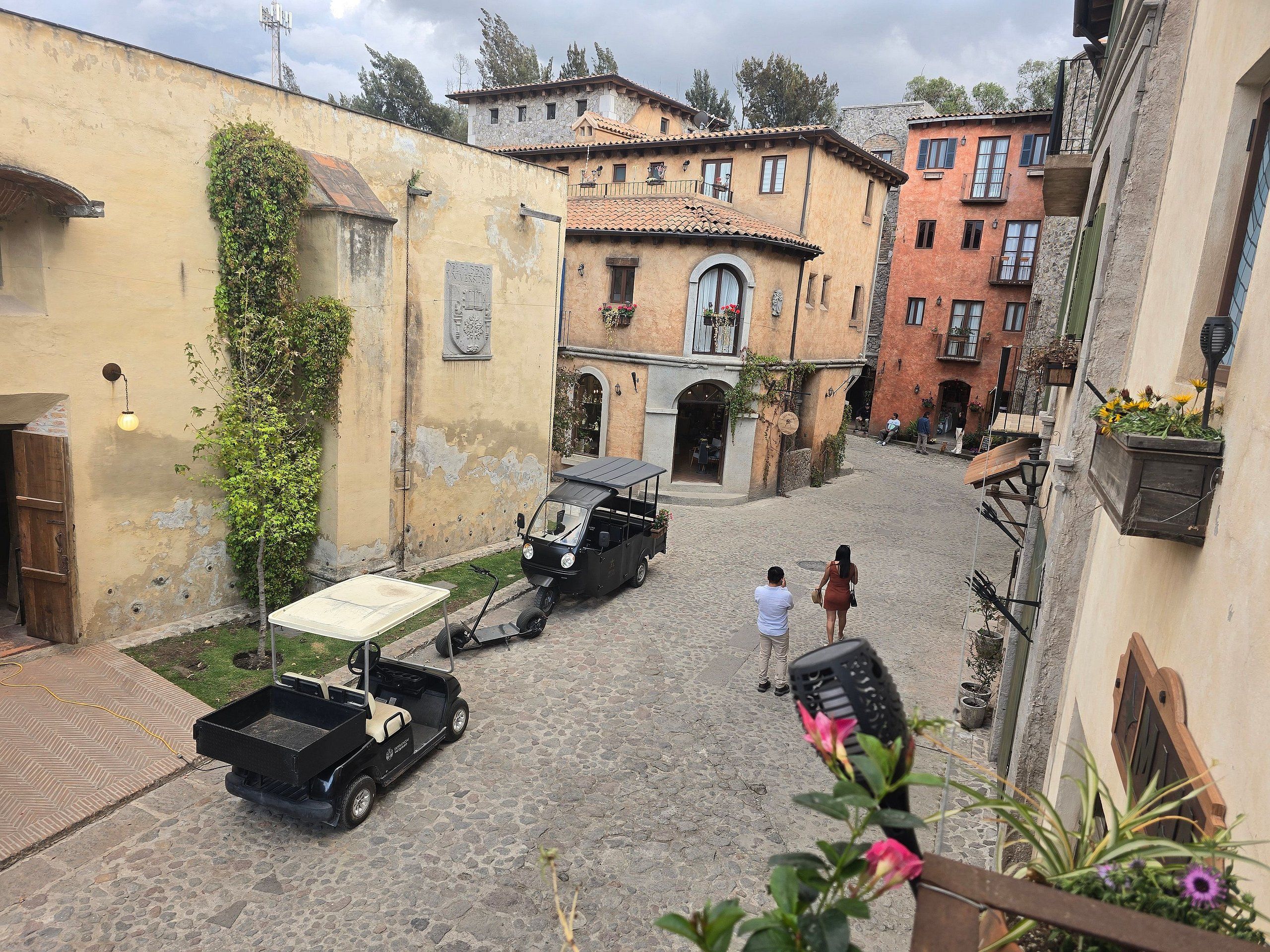 Una calle adoquinada en un pueblo histórico, con edificios de arquitectura tradicional, un carrito de golf y una persona caminando.