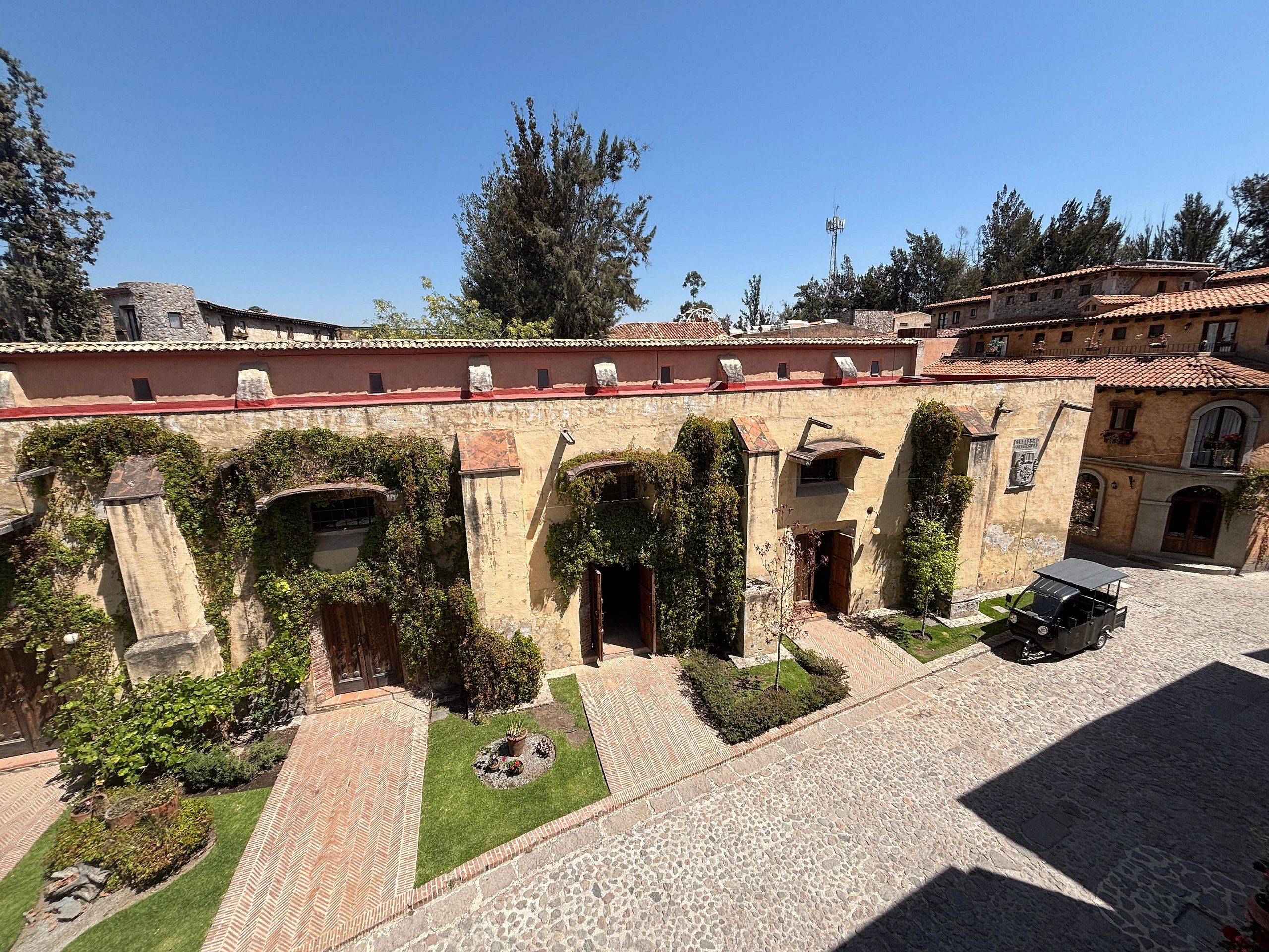 Um pátio com edifícios de pedra, portais em arco e uma área pavimentada com um veículo.