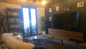 Una sala de estar con un televisor de pantalla plana grande, un mueble de entretenimiento de madera, un sofá con una manta blanca suave y una planta en maceta.