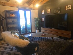A living room with a large flat-screen TV, a wooden entertainment unit, a sofa with a fluffy white throw, and a potted plant.