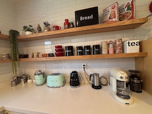 Una cocina con estantes de madera, un panero y varios electrodomésticos, como una cafetera y una licuadora.