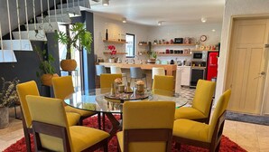 Una cocina moderna con armarios blancos, un refrigerador rojo y un comedor con una mesa de vidrio y sillas amarillas.