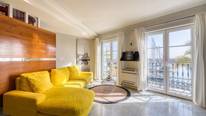 A bright living room with a yellow sofa, a round coffee table, and large windows with a view of a marina.