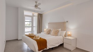 A modern bedroom with a bed, bedside tables, a ceiling fan, and a window with curtains. - Apartment in Playa de Mogán with Sea Views (Mogán)