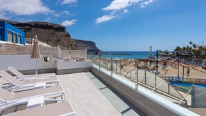 A rooftop terrace with sun loungers, a pool, and a view of the beach and ocean. - Apartment in Playa de Mogán with Sea Views (Mogán)