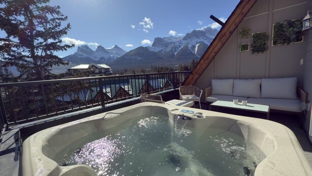 A hot tub on a balcony with a mountain view, a white sofa, and a table with two cups.